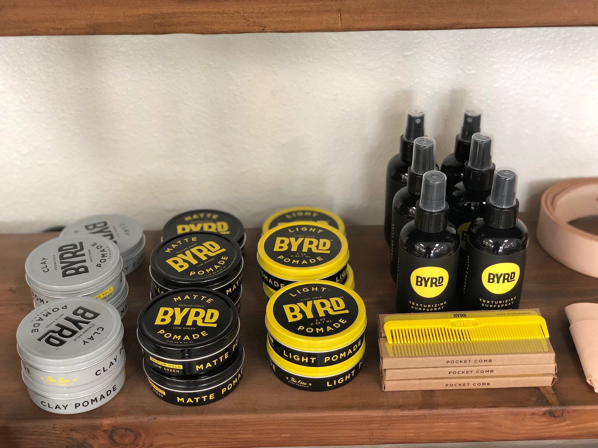 Collection of Byrd grooming products including pomades and sprays on a wooden shelf.