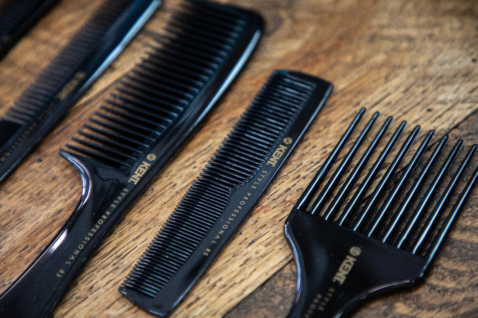Set of four black Kent professional hair combs neatly arranged on a barber station—premium-grade tools trusted for precision styling in barbershop environments.