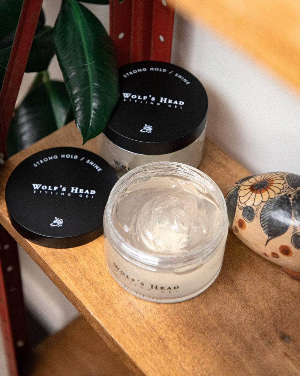 Wolf’s Head Styling Gel Pomade jars on vintage red retail shelf  with plant– strong hold high shine hair product. Open jar shoes gel detail.