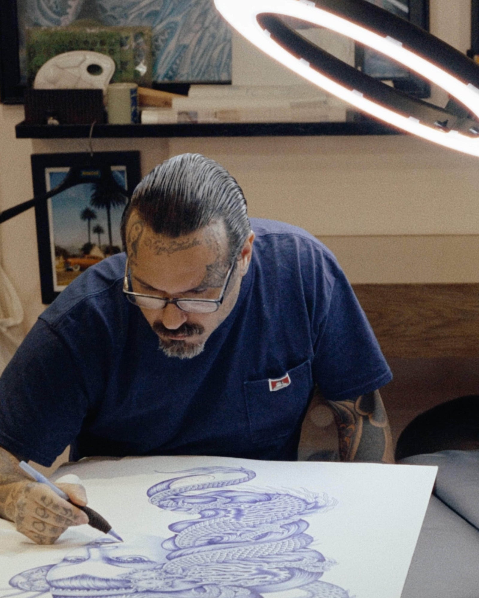 Wolf’s Head Styling Gel Pomade used in a slicked-back hairstyle on a tattoo artist mid-drawing—strong hold, high shine, water-based hair product for clean, precise looks.