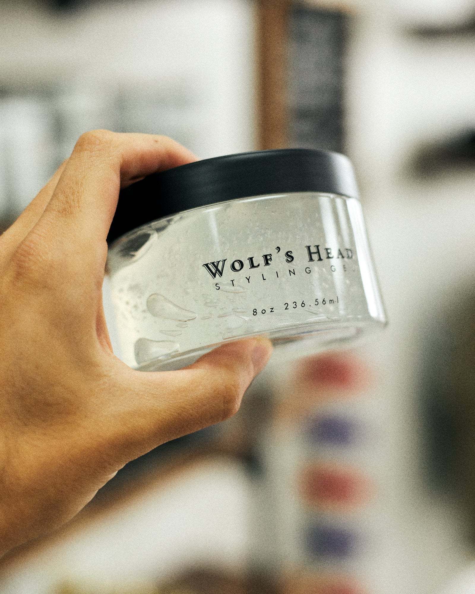 Close-up of a hand holding a jar of Wolf’s Head Styling Pomade, with a softly blurred background, premium men’s grooming product in focus.