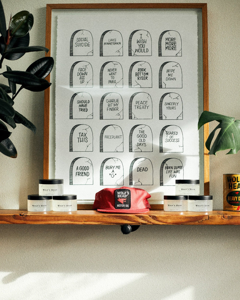 Wooden shelf display with Wolf’s Head pomade jars, a red cap, and framed prints— Strong Hold High Shine water based pomades