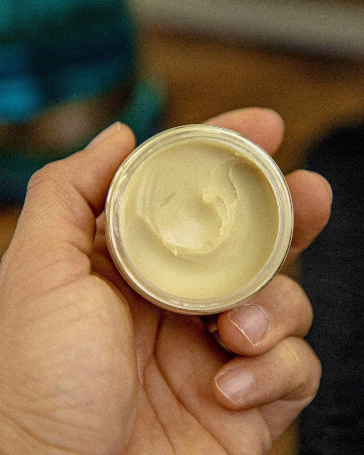 Hand holding a small container of cream with a blurred background