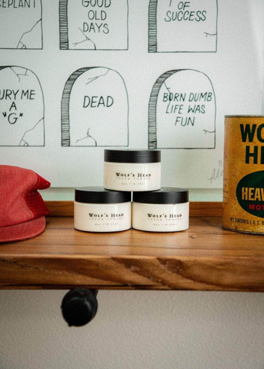 Wolf’s Head Cream Pomade jars and vintage Motor Oil display on wood shelf – medium hold matte finish grooming product
