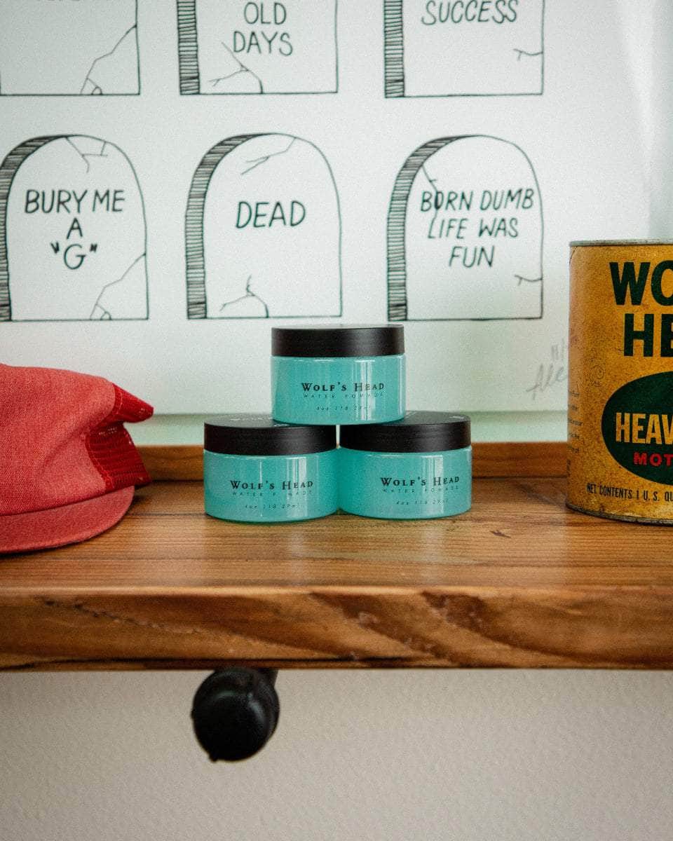 Wolf’s Head Water Soluble Pomade jars and vintage Motor Oil display on wood shelf – strong hold shine finish grooming product made in California