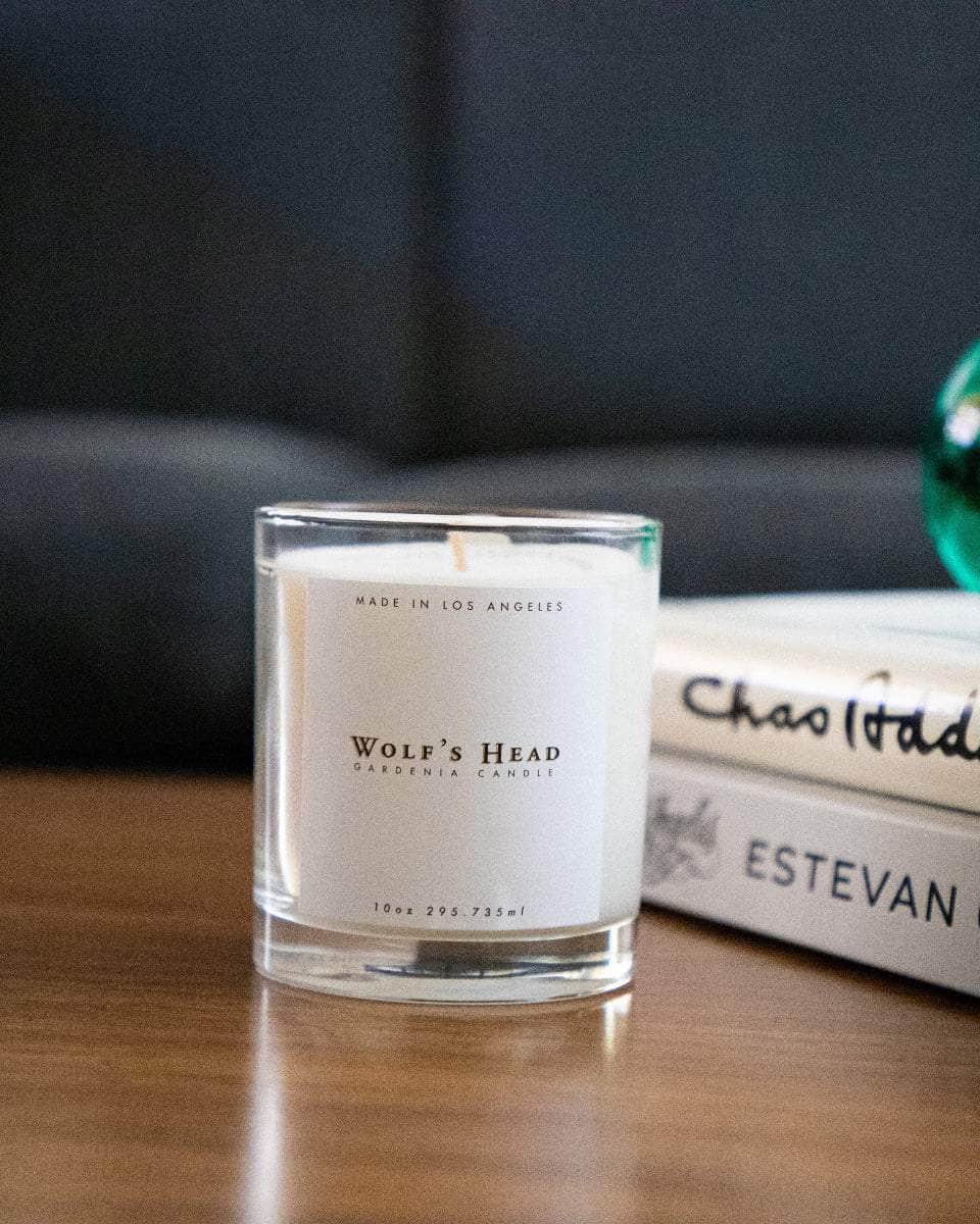 Wolf’s Head Gardenia Candle on a wooden table with art books and couch- natural, soy-based candle with a long lasting burn and subtle floral scent. A California-made essential for refined, everyday atmosphere.